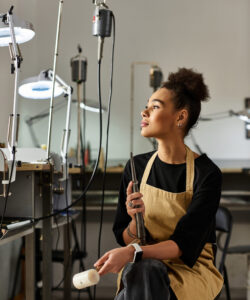 The artisan enjoys a moment of contemplation surrounded by tools and jewels in her workshop.