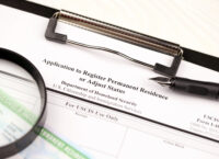 I-485 Application to register permanent residence or adjust status form and green card from dv-lottery on A4 tablet, lies on office table with pen and magnifying glass close up