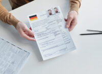 High angle shot of man applying for travel visa in embassy or consulate giving paper form with photos