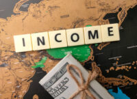 Toys word and banknotes with the word INCOME on a world map background.