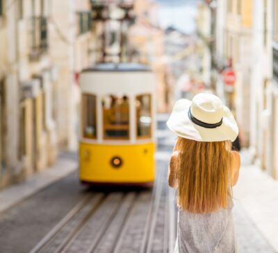 Young woman tourist photographing famous retro yellow tram on the street in Lisbon city, Portugal